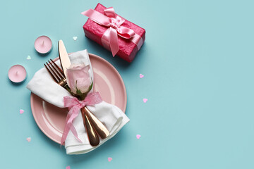 Table setting for Valentine's Day with rose, candles and gift on blue background