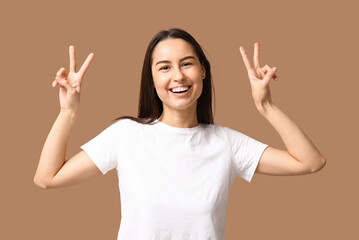 Beautiful young woman showing victory gesture on beige background
