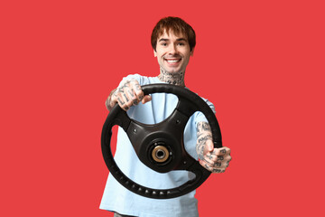 Handsome young man with steering wheel on red background