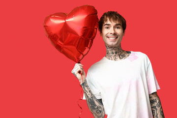 Handsome young man with heart-shaped air balloon on red background