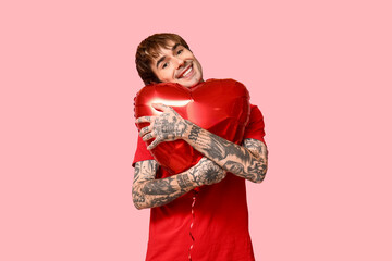 Handsome young man with heart-shaped air balloon on pink background