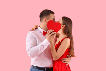 Lovely couple with heart-shaped gift box kissing on pink background. Valentine's Day celebration