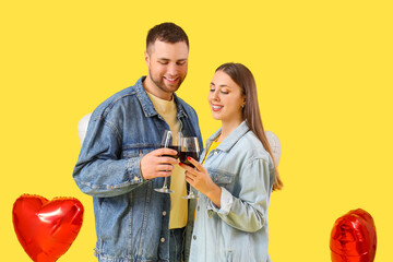 Lovely couple with glasses of wine and heart-shaped balloons on yellow background. Valentine's Day...