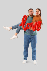 Obraz premium Lovely couple with word LOVE made from balloons on grey background. Valentine's Day celebration