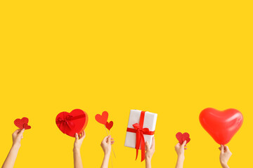 Female hands with gift boxes and heart shaped air balloon on yellow background. Valentine's Day...