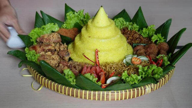 Yellow rice in a cone shape. In Indonesia called "Nasi Tumpeng". A festive Indonesian rice dish with side dishes. Tumpeng rice in a bamboo woven tray.