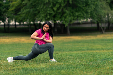 beautiful brunette latina woman doing stretching, yoga and exercises, in a green grass park wearing sports clothing