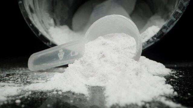 On a Black Background, White Powder is Sprinkled from a Measuring Spoon. Jar in the Background. Dolly slider, close up.
