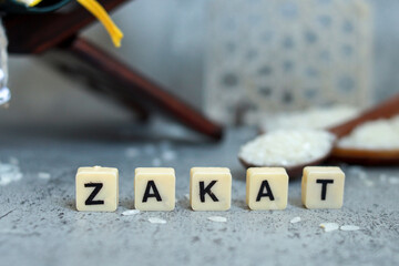 Word Zakat is written on the white cubes with rice grain on wooden spoon. Islamic donation concept