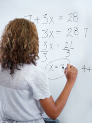 Woman, teacher and writing on whiteboard for mathematics, numbers or equations in classroom. Rear...