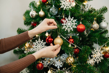 Young woman's hand decorating Christmas tree indoors.