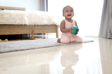 Happy smiling African cute toddle baby infant kid holding toy while crawling on floor in bedroom at...