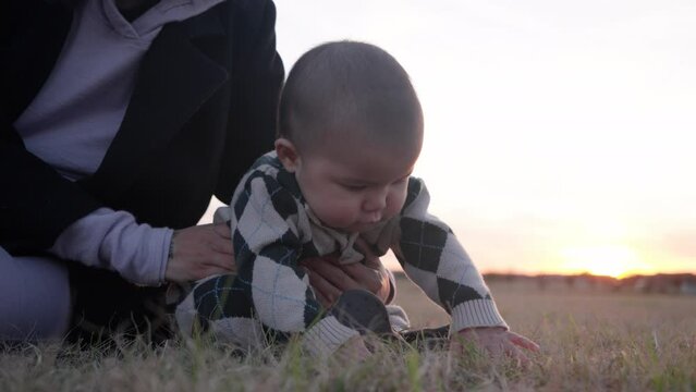 Cute Asian baby feeling and touching grass with his hands in a park at sunset. Slow motion