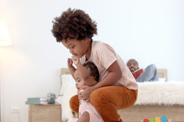 Happy African family spending time together, brother boy with black curly hair try to hold and lift...