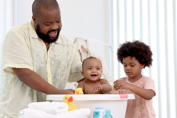 Happy African family, father bathing kid in tub, dad and son brother washing and cleaning little...