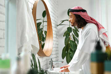 Young Arab man getting ready and looking at the mirror in the bathroom