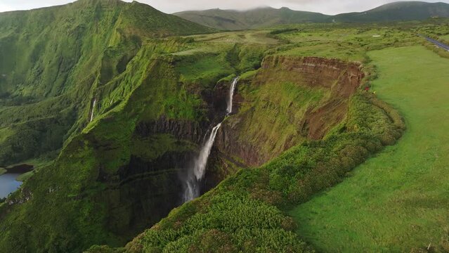 Big waterfall lot of power in middle of lush green vegetation in Azores, aerial