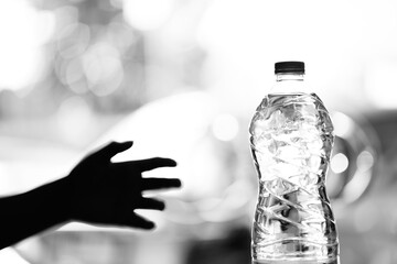 The shadow of a hand reaches towards a bottle of water. black and white scene concept photo, Don't...