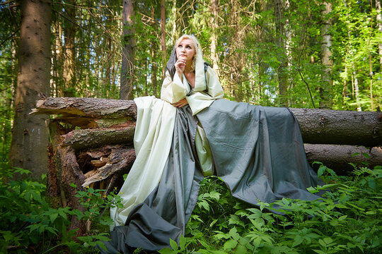 Adult mature woman 40-60 in a green long fairy dress in forest. Photo shoot in style of dryad and queen of nature. Fairy who loves nature in beautiful green summer forest. Concept of caring for nature