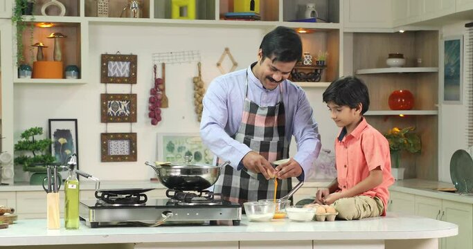 Video of Indian father and son baking in kitchen breaking eggs into mixing  bowl
