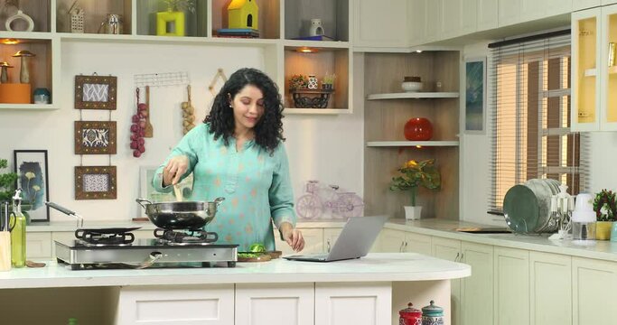 Happy woman watching video recipe on laptop while cooking  healthy lunch in kitchen using laptop
