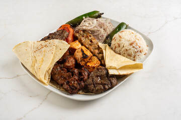 Mixed grill made of meat, chicken and fried quiche, served on a white plate with delicious baldo rice and fried potatoes.