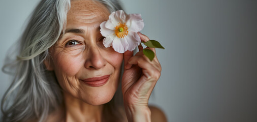 Portrait of a beautiful elderly woman with grey hair with a flower, smiling looking at camera, showing aging skin with fine lines and pigmentation, Asian ethnicity, closeup photo