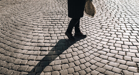 Two women's legs in black jeans and winter boots walk along gray granite paving stones and casts a contrasting shadow. The concept of a walk in the old city. Lviv, Ukraine.
