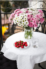 a plate of strawberries and a bouquet of flowers on a table with a white tablecloth on the balcony
