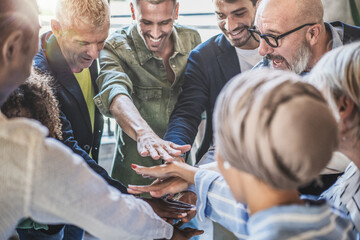 Diverse business team stacks hands in unity, showcasing teamwork and partnership in a dynamic workplace.