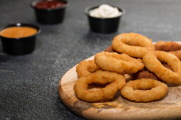 Crunchy Onion Rings with dip sauce and mayonnaise isolated on wooden board with dip sauce top view of grill food on dark grey background