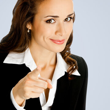 What about You? Smiling woman in black suit pointing forefinger at viewer, copy space for text. Business concept. Grey background. Brunette businesswoman. Square composition