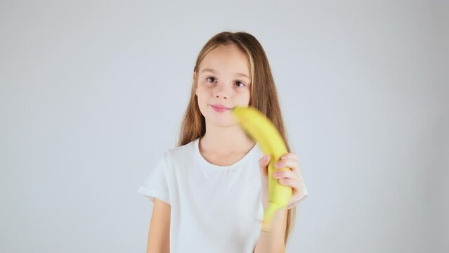 Close-up preteen girl enjoying healthy food. Portrait little girl in her 7 holding delicious banana with white isolated background