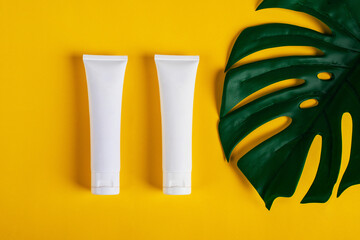 Cosmetic product in tube, bottle, lotion or serum on yellow background and tropical monstera leaves. 