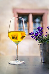 A glass of local white wine at an outdoor restaurant with blurred half timbered houses in Riquewihr, France, a village on Alsatian Wine Route