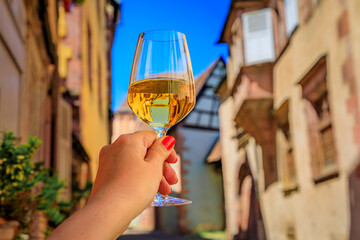 Woman s hand with a glass of white wine at an outdoor restaurant, blurred half timbered houses in Riquewihr, France, a village on Alsatian Wine Route