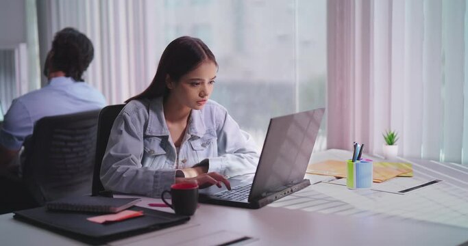 Indian Hindu gen z young adult woman lady sitting desk chair use laptop look screen work online check email task indoor office Hindu India teen female girl read good news feel great get new job deal