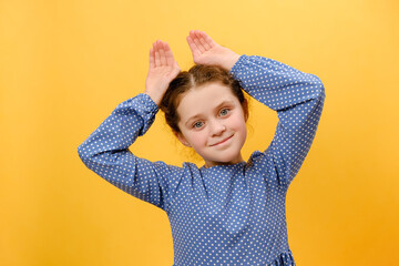 Portrait of lovely funny preteen girl kid smiling friendly and doing bunny ears gesture on head,...