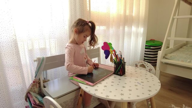 Cute little girl enjoys painting. Girl drawing and coloring picture on tablet in her room at home