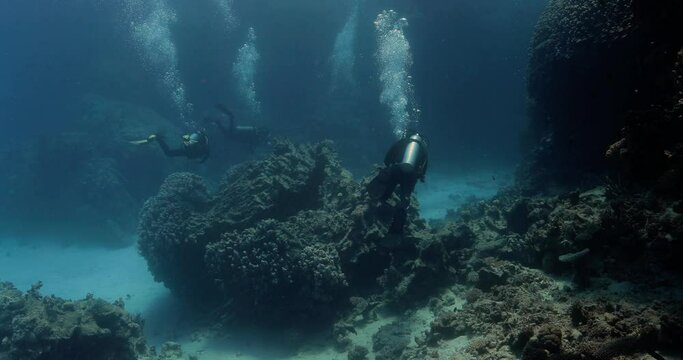 three divers roaming around a huge rock in the ocean