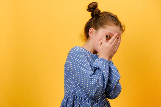 Portrait of shocked little girl kid covers face with hands, posing isolated over yellow background, child watching horror film, movie, reaction, facial expression. Children and human emotions concept