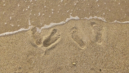 Footprints of a husband and wife on the white sand of the beach. Simple romantic holiday background concept