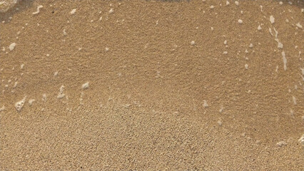 Golden sand with small waves on the beach. Top view with texture, great for holiday background