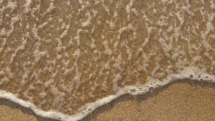 Golden sand with small waves on the beach. Top view with texture, great for holiday background