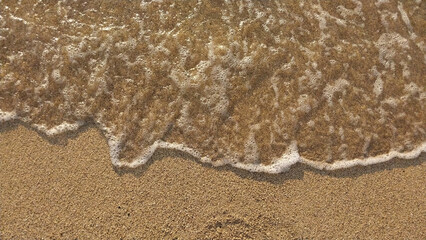 Golden sand with small waves on the beach. Top view with texture, great for holiday background