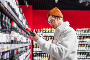 Man in store choosing alcohol. Guy reads label on bottle of wine in liquor section. Holidays...