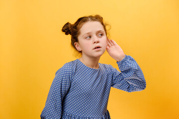 Portrait of excited caucasian preteen girl child overhearing tattles, listening with hand near ears to side, posing isolated over plain yellow color background wall in studio. Kids curiosity concept - Powered by Adobe