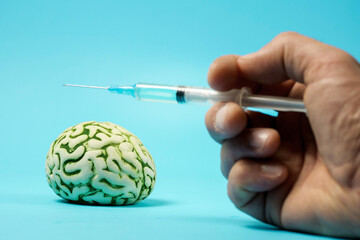 Hand holding injector with liquid over abstract human brain on blue color background. Drug addiction and use concept. Medical healthcare theme. Copy space.