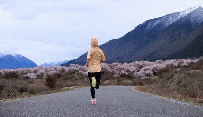 Woman running in spring tibet,peach flowers blooming and snow capped mountains in the background, China