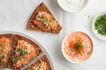 Appetizer with red caviar, sour cream, dill, onion and rye bread on the white table - the finnish recipe for a holiday food, flat lay in minimalistic style